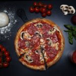 A mouth-watering pepperoni pizza surrounded by fresh ingredients on a dark background. - Photo by Antonio Di Giacomo on Pexels
