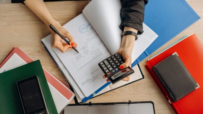 Accountant analyzing financial documents with a calculator on a desk, highlighting business tasks. - Photo by Mikhail Nilov on Pexels