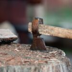 Close-up of an axe stuck in a tree stump with firewood beside it. - Photo by Filip Marcus Adam on Pexels