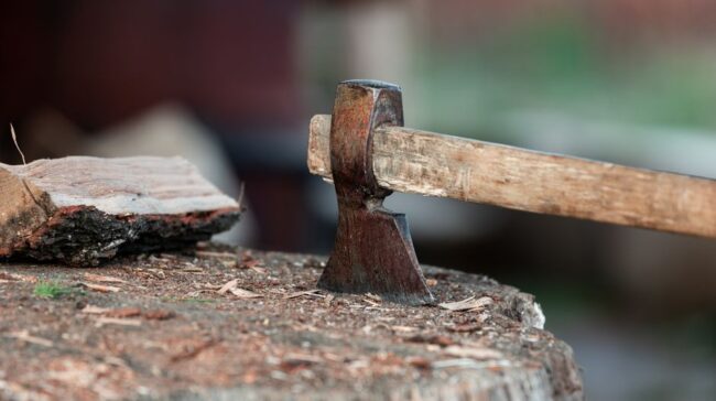 Close-up of an axe stuck in a tree stump with firewood beside it. - Photo by Filip Marcus Adam on Pexels