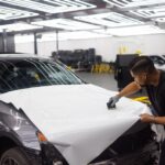 Man applying vinyl wrap on car hood in an automotive workshop setting. - Photo by Auto Records on Pexels