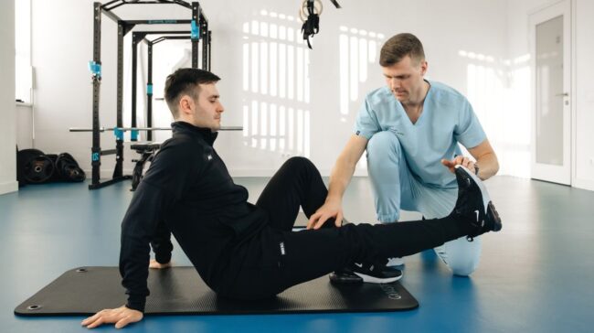 A physiotherapist assists a male patient during a rehabilitation session in a modern clinic. - Photo by Funkcinės Terapijos Centras on Pexels