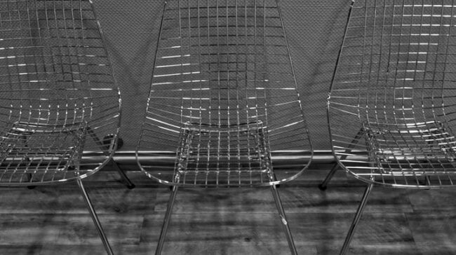 Three metal wire chairs aligned indoors against a textured wall. - Photo by Hajo Merz on Pexels